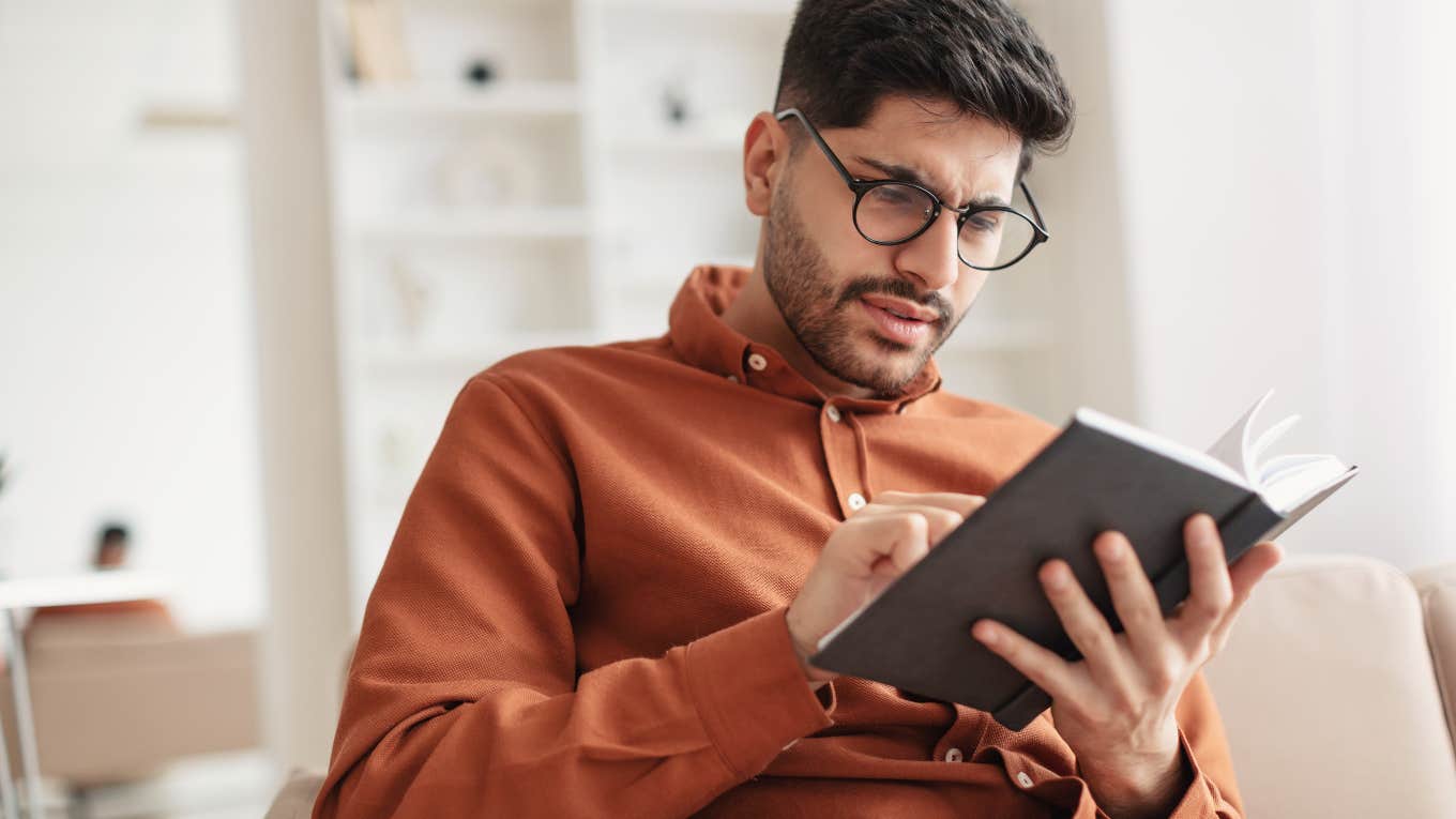 focused young man reading journal while sitting on couch in home