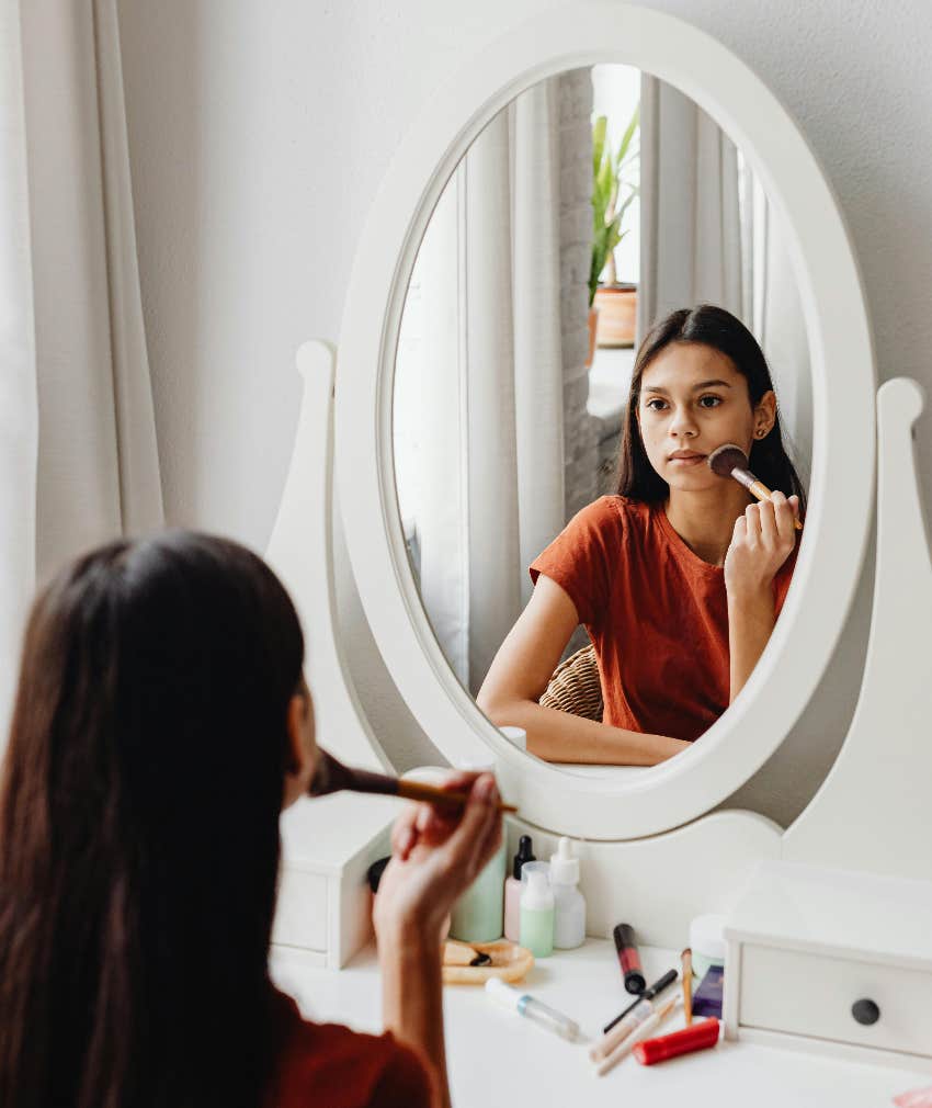teen girl applying makeup in the mirror