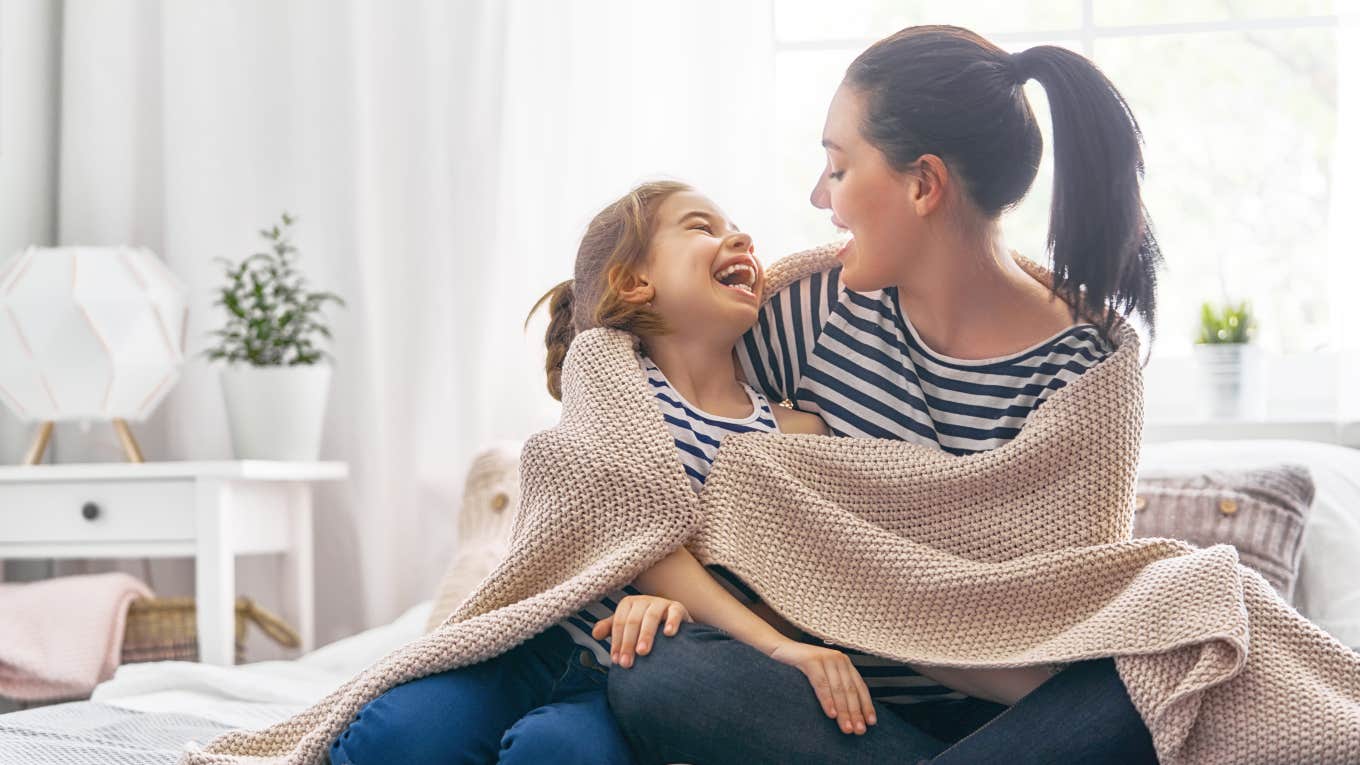 mom and daughter laughing together wrapped up in a blanket