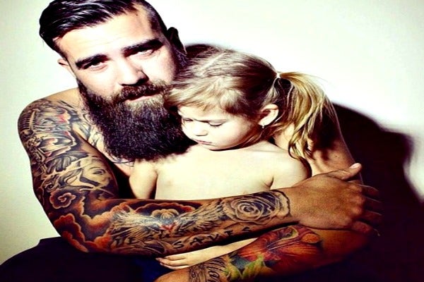 Man with beard, and tattoos with daughter in his arms.