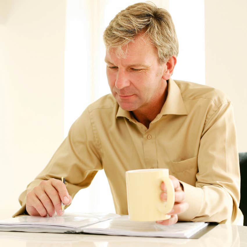 man looking through documents holding a cup of coffee