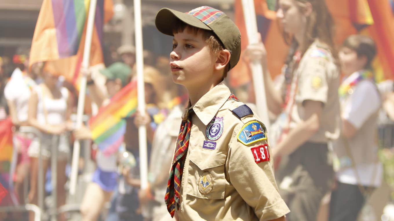 Boy scout holding LGBTQ+ flag while walking in a parade. 