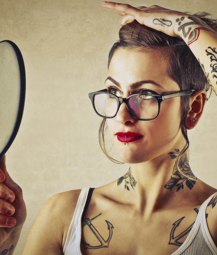 woman with tattoos and piercings looking in mirror