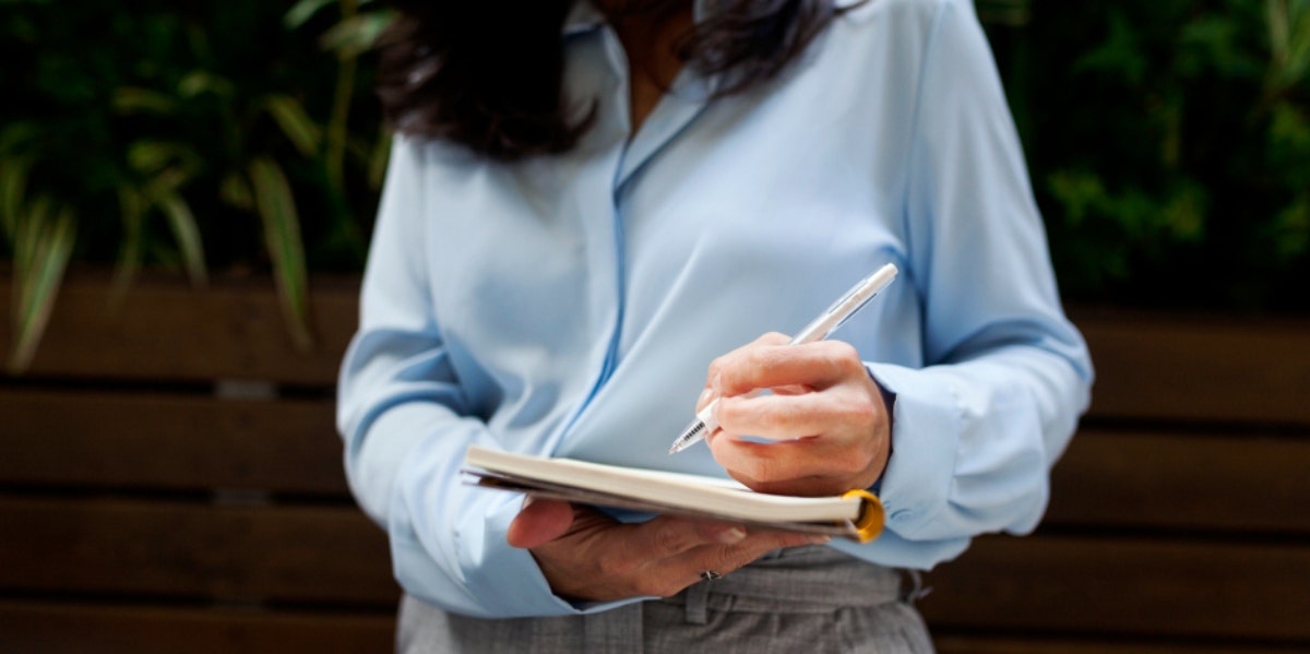 woman in business attire writing in a notebook