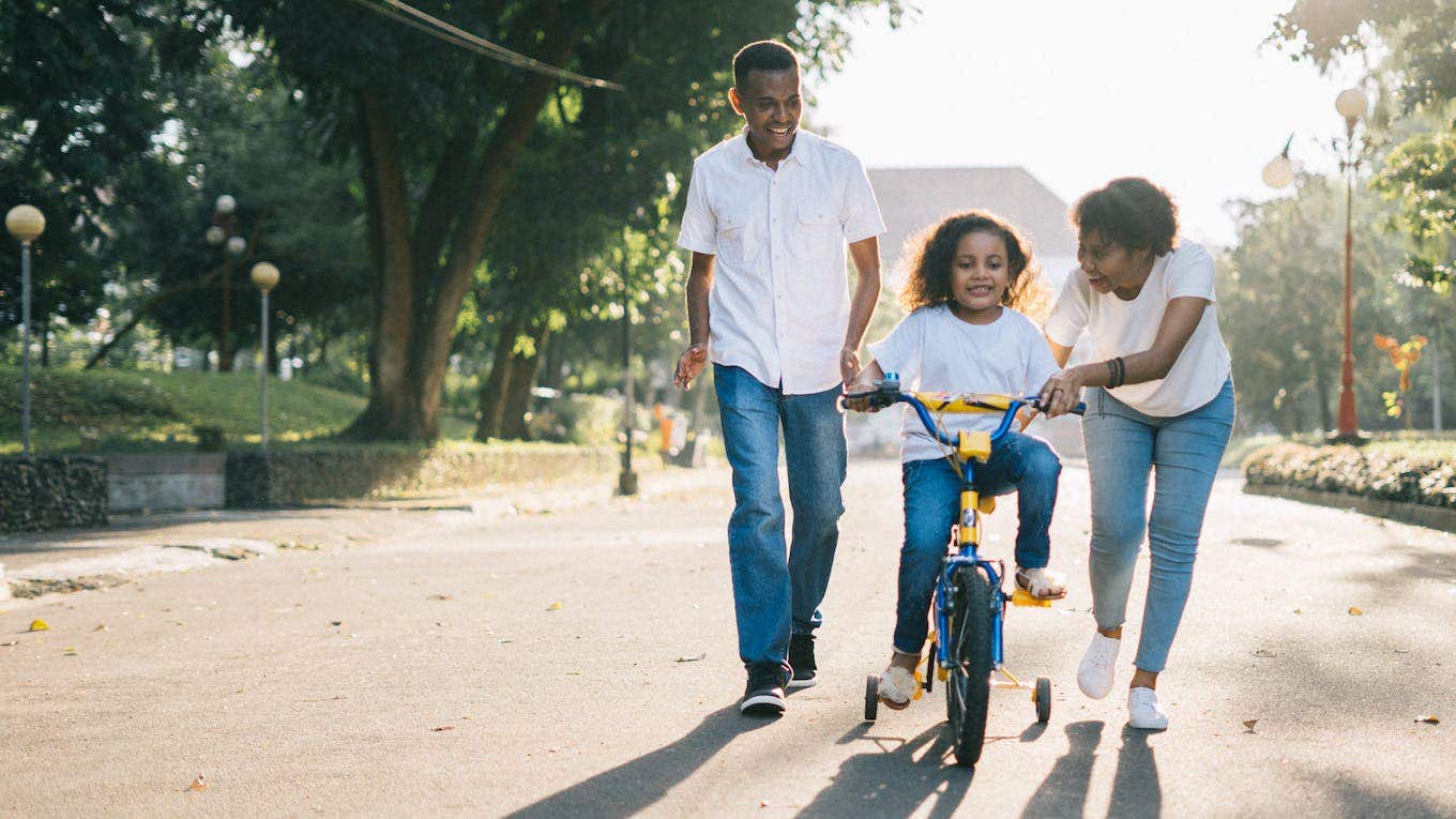 parents teaching daughter to ride a bike