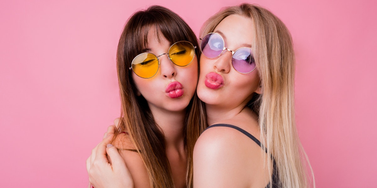 two friends making kissy faces pink background