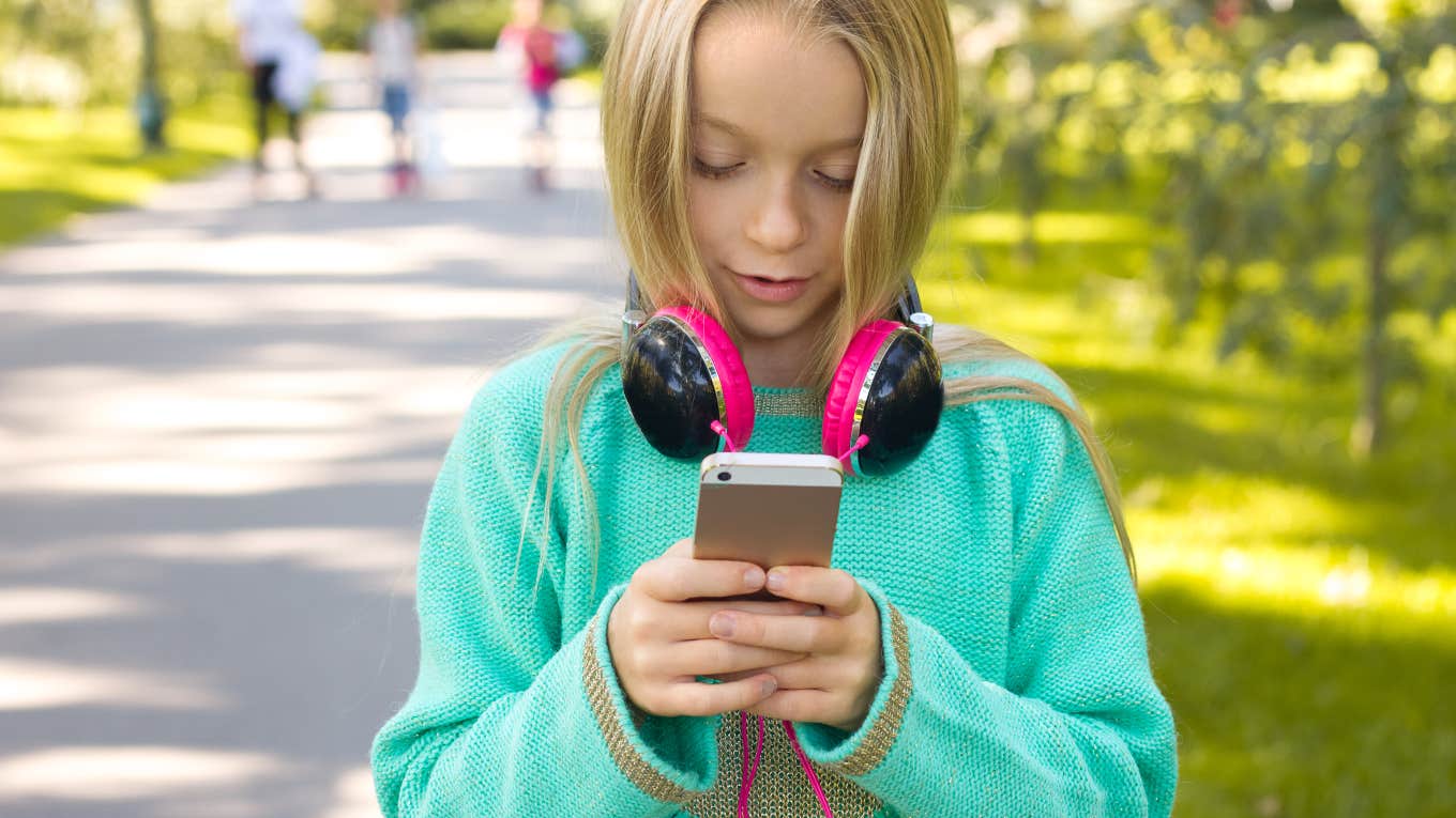 little girl looking at phone with headphones on