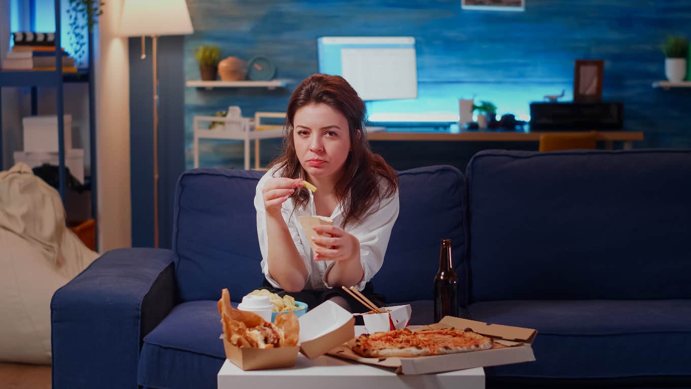 sad woman sitting on the couch eating junk food