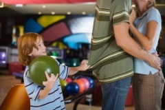 mom and dad kissing with child watching at bowling alley