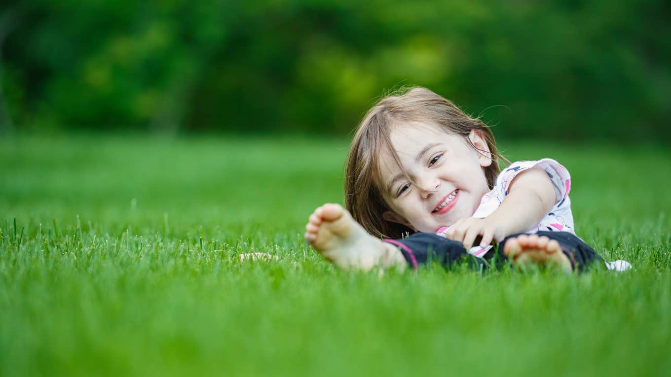 little girl laying in grass barefoot