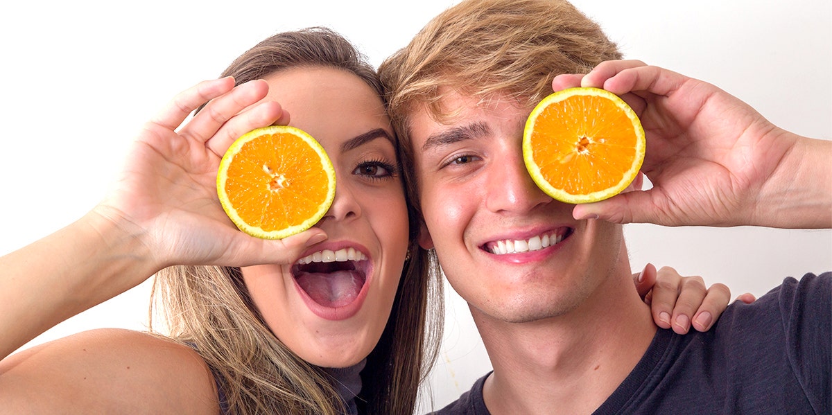 Young blonde woman and young blonde man holding oranges over their faces