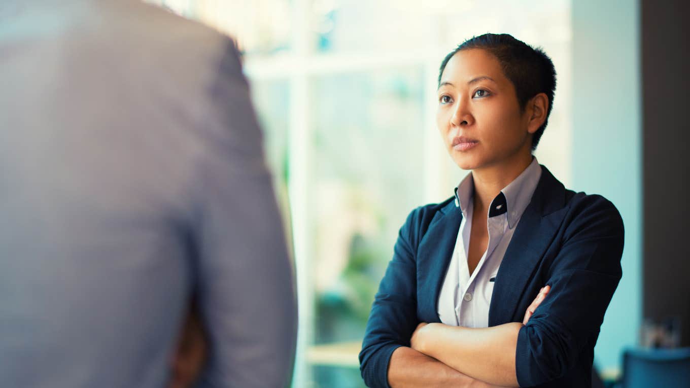 Tense Asian businesswoman looking at male partner with crossed arms