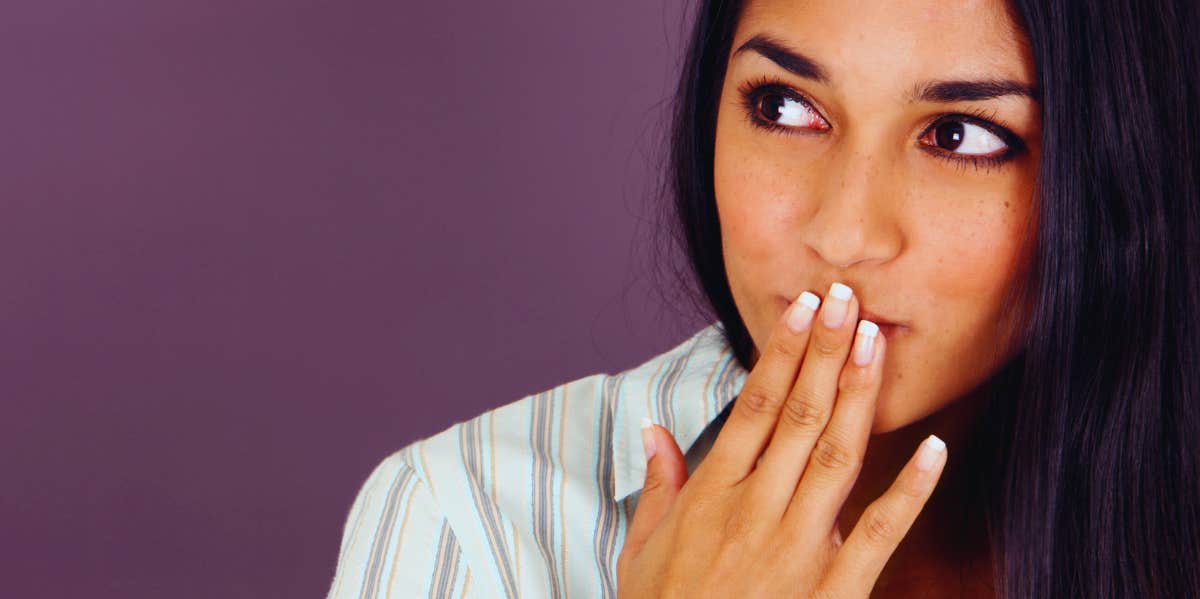 woman in front of purple background with hand over her mouth looking to the side