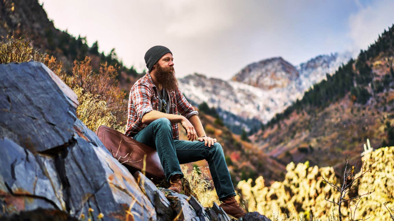 Bearded man sitting in the mountains on a rock