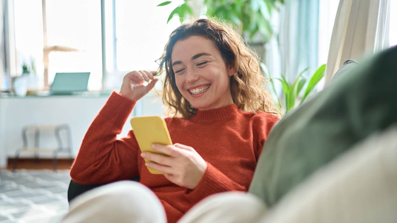 smiling woman on couch scrolling through phone
