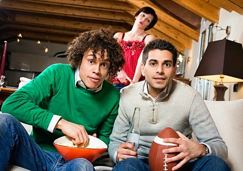 Two men watch football with woman in the background