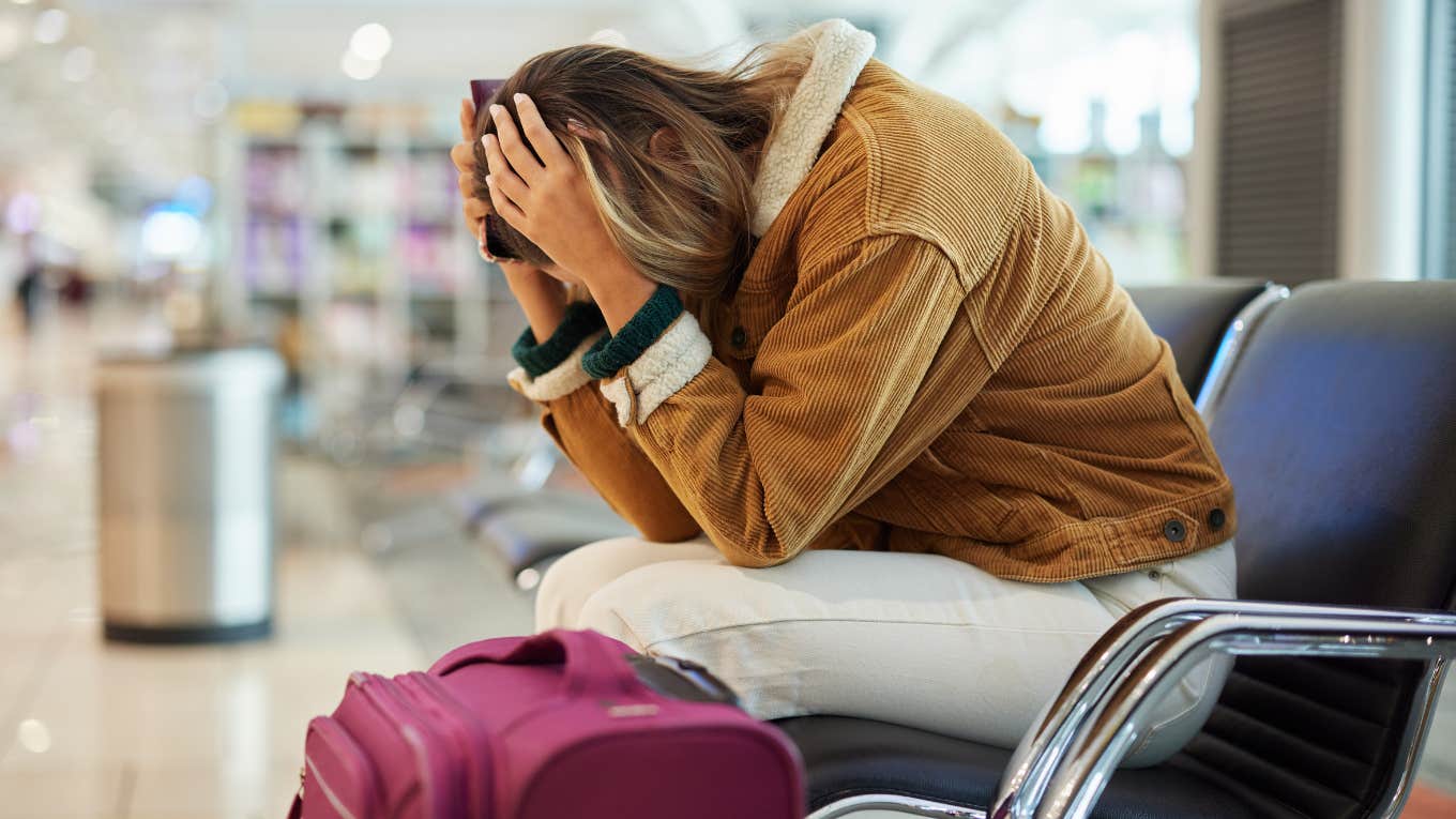 upset woman sitting in airport terminal with head in hands