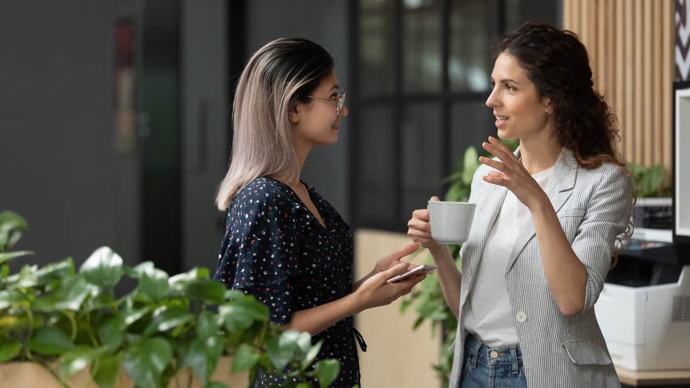 Two young business women chatting during work break standing in modern office