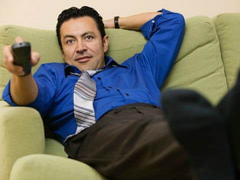 man wearing a tie on the sofa with a TV remote