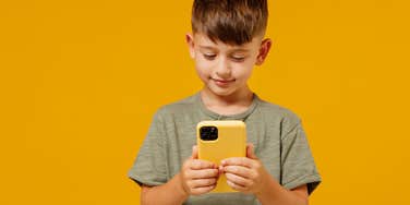 little boy on phone in front of orange background