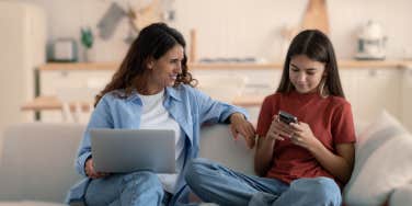 mom and teen daughter on the couch talking while teen looks at phone