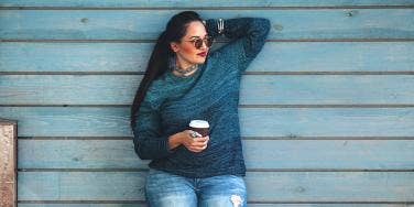 woman holding coffee standing against wall