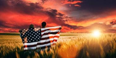 couple holding American flag watching sunset