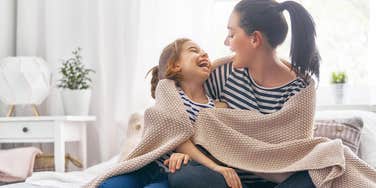 mom and daughter laughing together wrapped up in a blanket