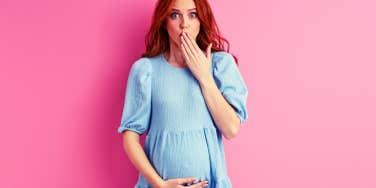 pregnant woman looking surprised in front of pink background
