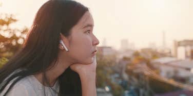 A young woman sits on a rooftop while listening to music