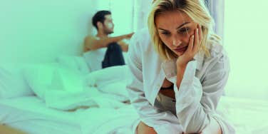 unhappy girl sitting on bed with boyfriend behind her