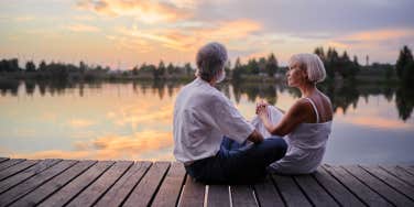 middle-aged couple sitting together on lake bank enjoying beautiful sunset