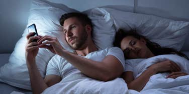 husband on the phone with his co-worker in bed while next to sleeping wife