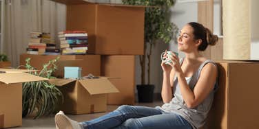 woman sitting on floor with coffee mug in hand surrounded by moving boxes