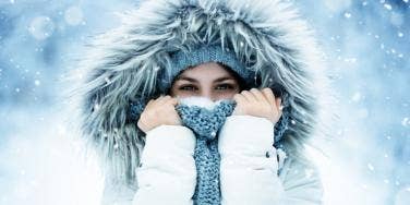 woman stands in the snow wearing a fur hood and covering her face