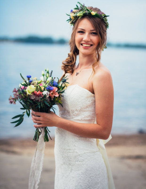 bride on her wedding day holding flowers by the water