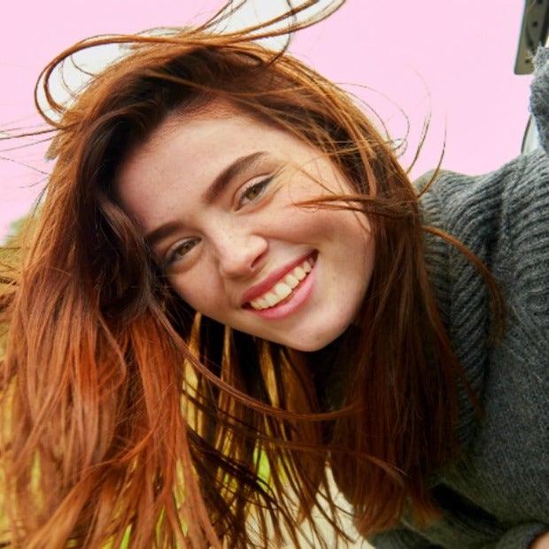 young woman with auburn hair smiles into the camera in a hopeful, romantic way