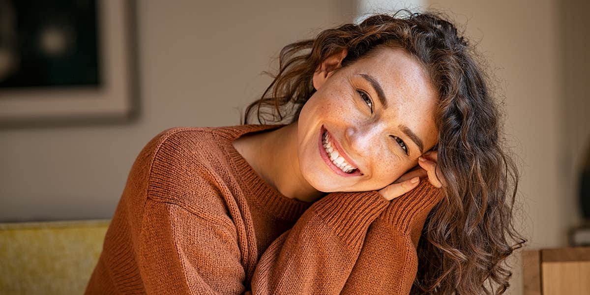 Happy young woman sitting on sofa at home and looking at camera.