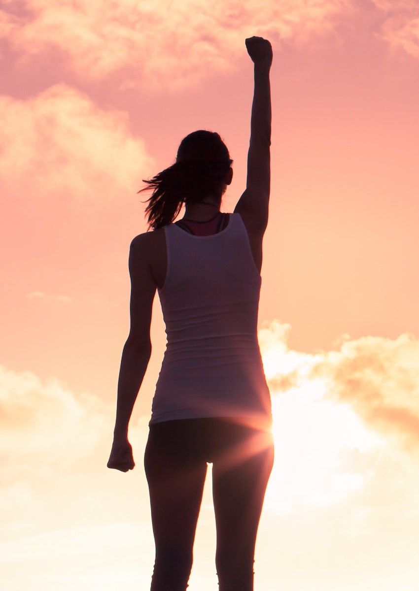 empowered woman with fist raised to the sunset sky