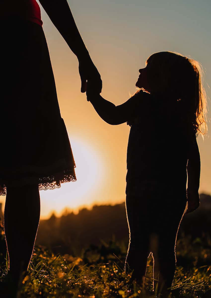 daughter holding mothers hand as they walk into the sunset