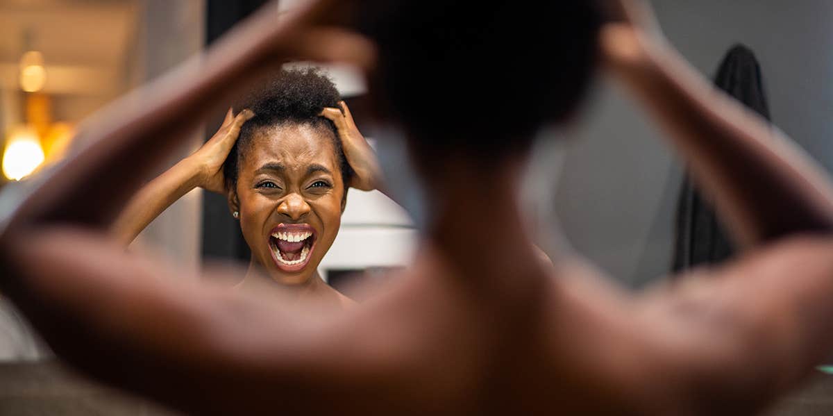 Portrait from back of young african american woman adjusting hair in mirror and shouting