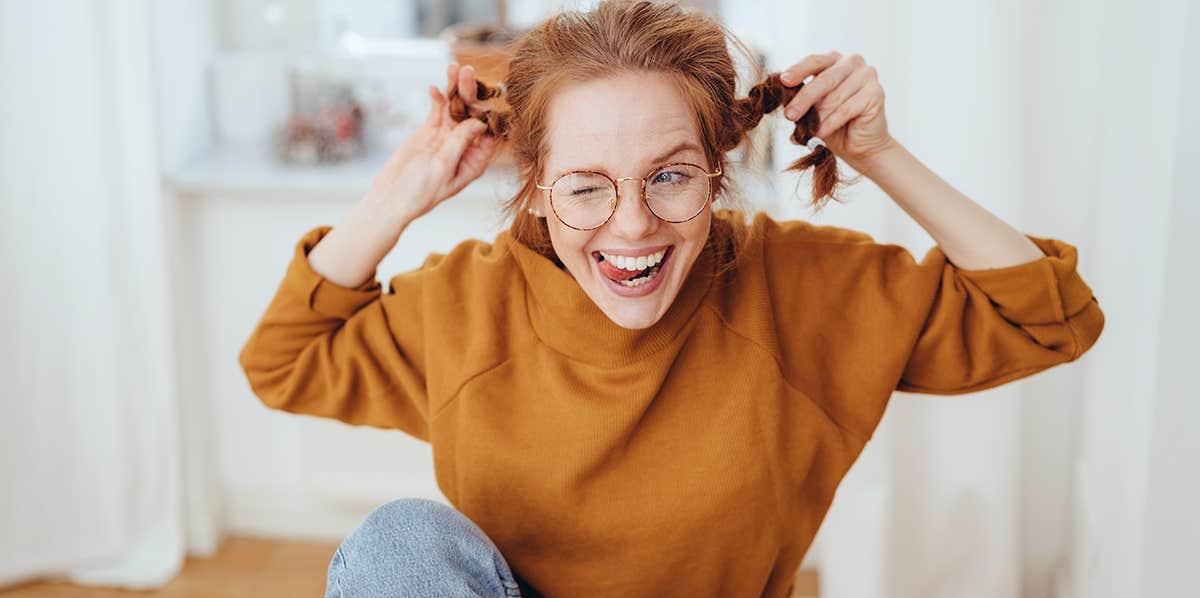 Cute mischievous young redhead woman pulling her pigtails while winking and sticking out her tongue with a teasing expression