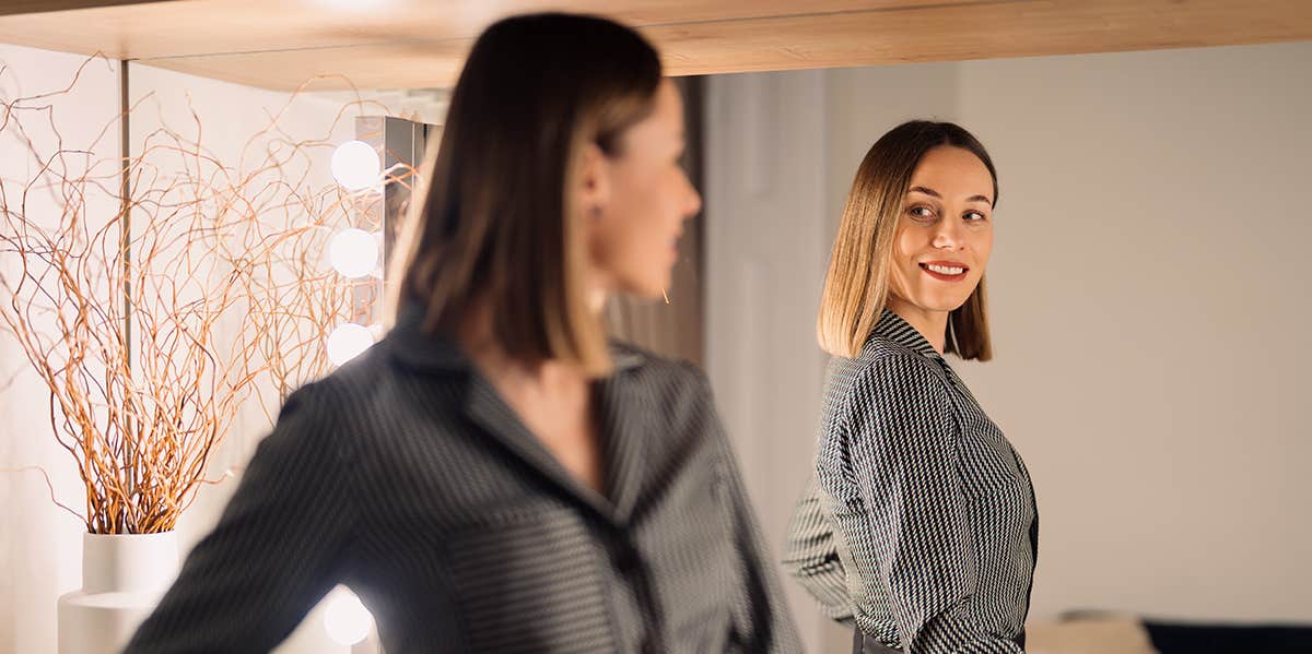 Self-confident Woman looking at her reflection into the mirror indoors