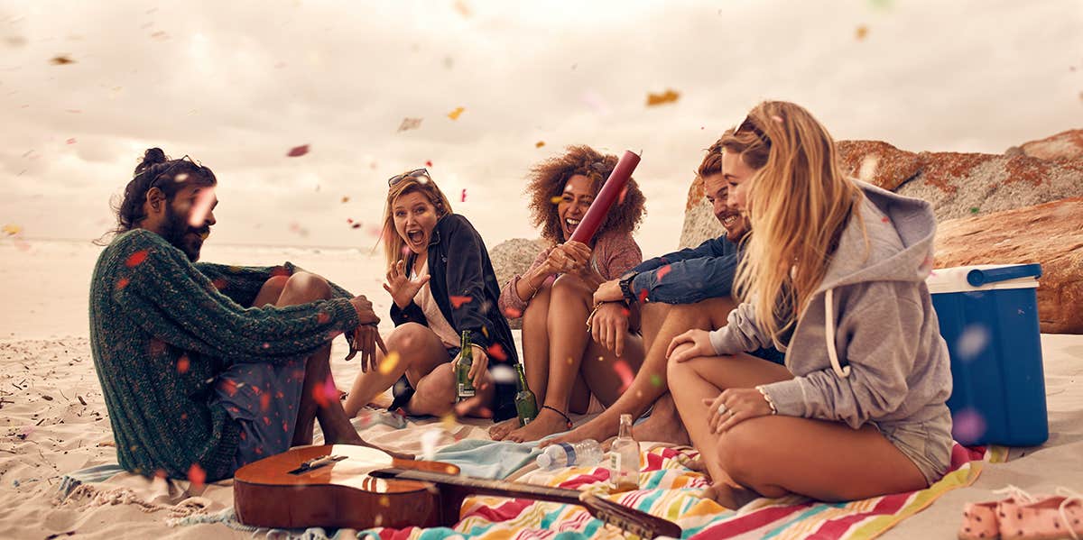 Happy friends partying on the beach with drinks and confetti.