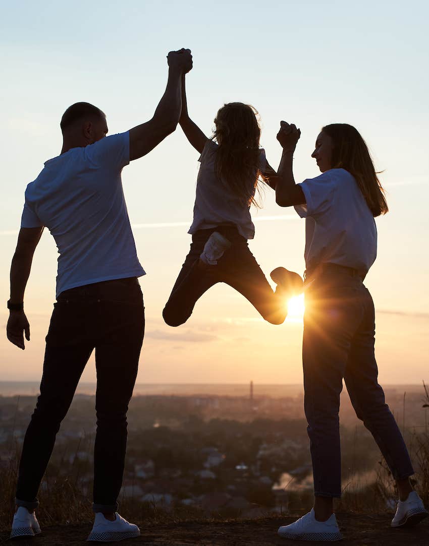 parents lifting child up at sunset