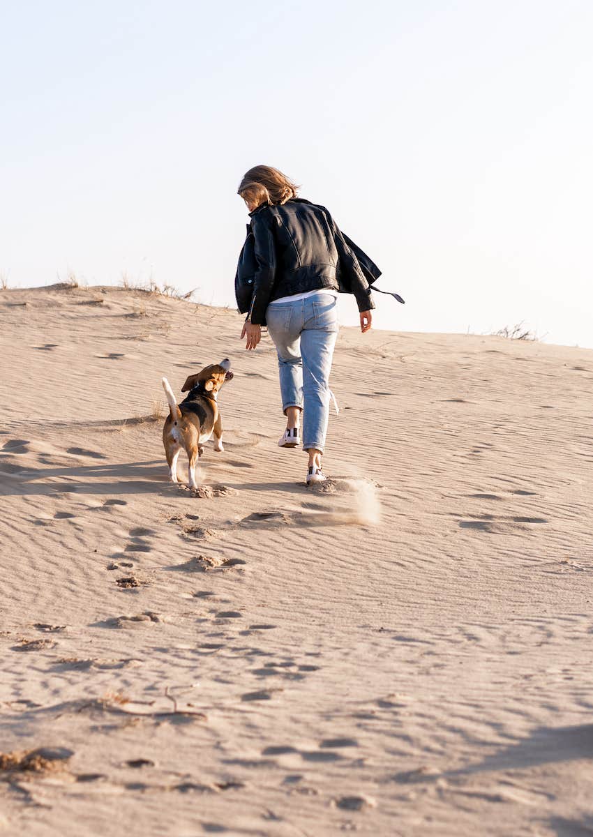 woman and dog run on beach