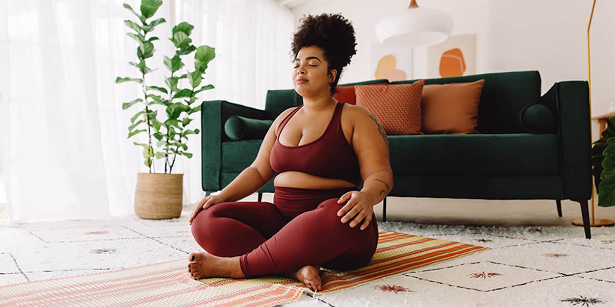Plus size woman sitting cross legged and closed eyes in living room.