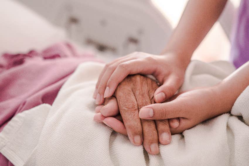woman holding elderly person's hand in hospital bed
