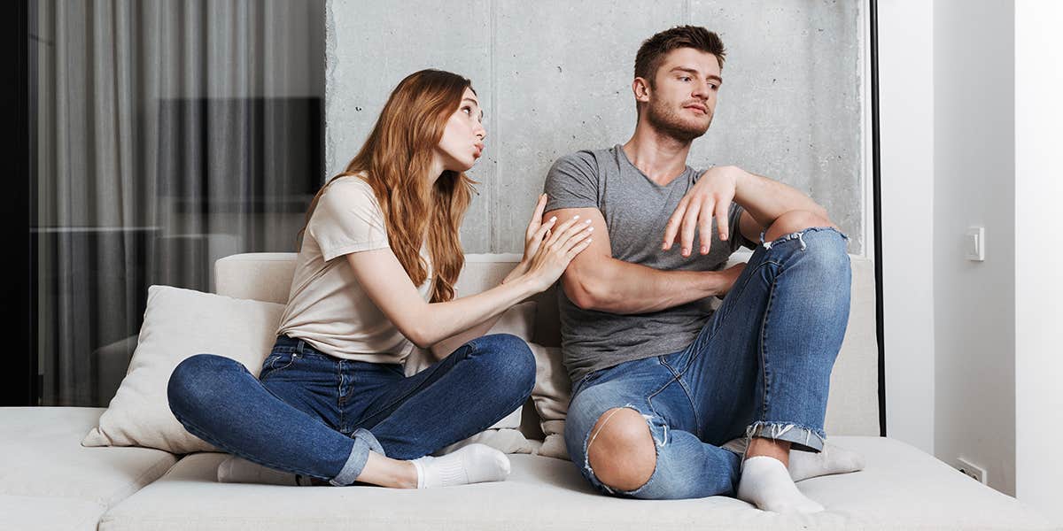 Pretty young woman trying to kiss her boyfriend while sitting together on a couch at home