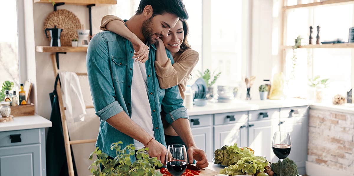 man and woman in kitchen embracing while he cooks